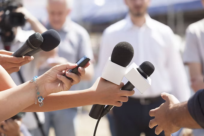 People at a press conference with hands holding microphones
